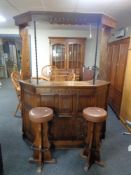 A shaped heavily carved oak bar with canopy together with a pair of leather seated bar stools