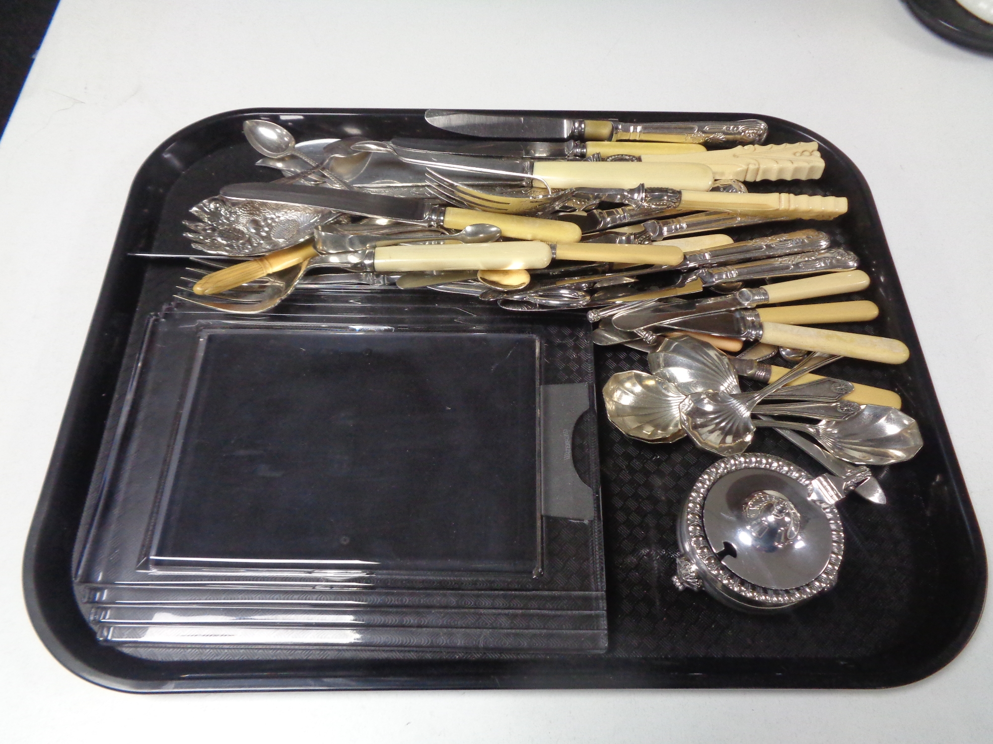 A tray containing assorted stainless steel and plated cutlery servers, plated mustard pot,