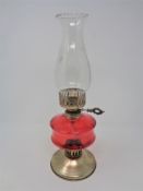 An oil lamp with red glass reservoir and chimney