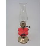 An oil lamp with red glass reservoir and chimney