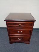 A three drawer glass topped bedside chest in a mahogany finish