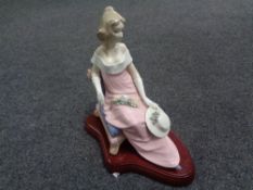 A Spanish figure, lady in pink dress seated on wooden plinth.