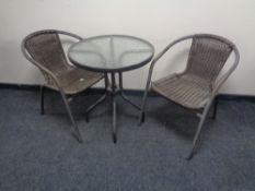 A circular metal glass topped bistro table and two metal and rattan armchairs