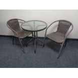 A circular metal glass topped bistro table and two metal and rattan armchairs