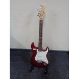 A Squier by Fender Strat electric guitar, red, together with a folding guitar stand.