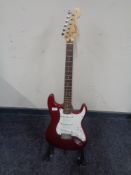 A Squier by Fender Strat electric guitar, red, together with a folding guitar stand.