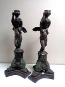 A pair of cast metal candlesticks depicting a cherub standing on a plinth, height 67 cm.