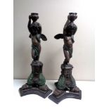 A pair of cast metal candlesticks depicting a cherub standing on a plinth, height 67 cm.