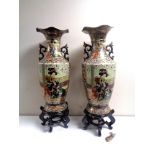 A pair of Japanese twin handled vases depicting geisha, on stands,