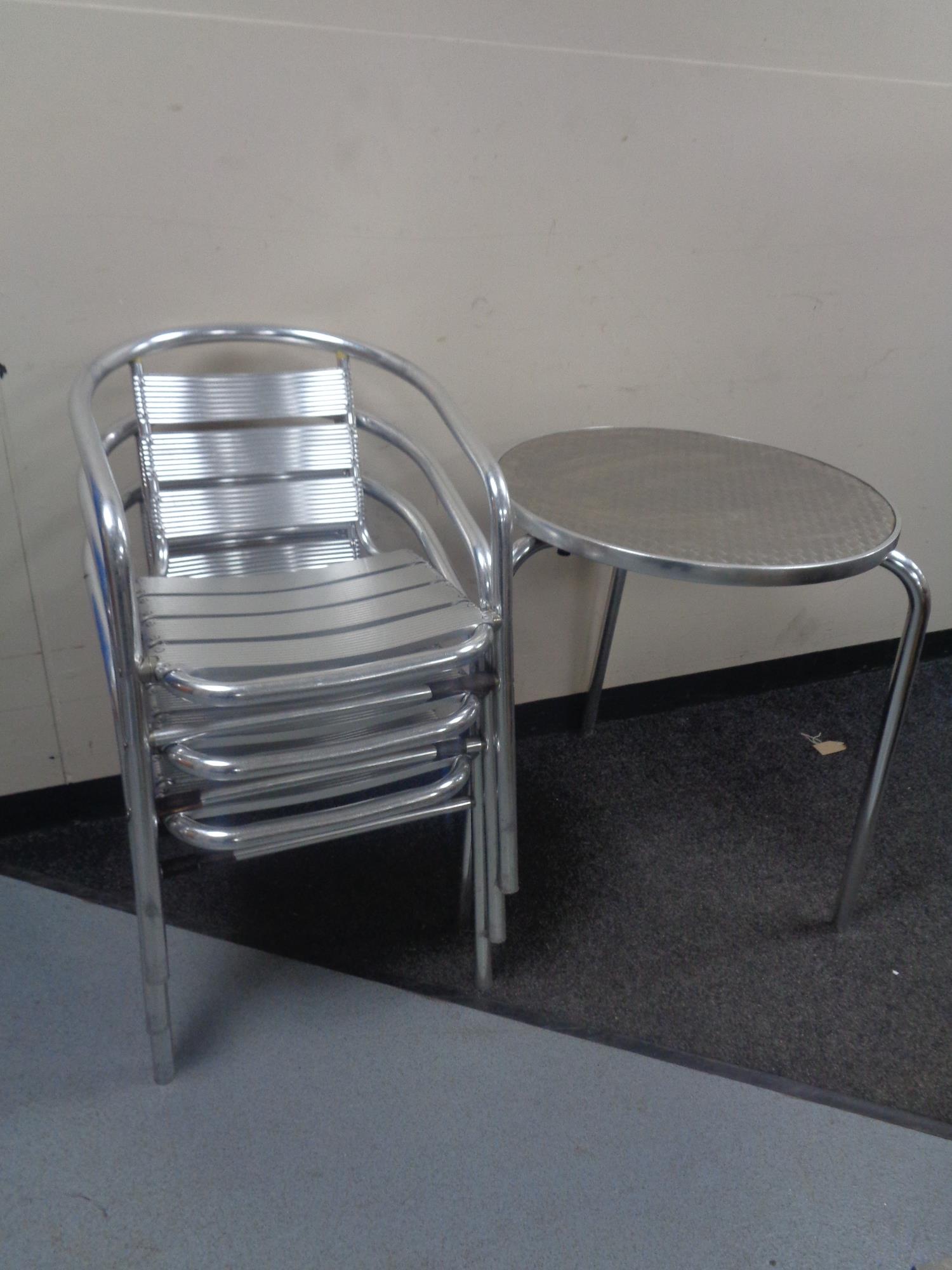 A circular metal bistro table together with six stacking armchairs