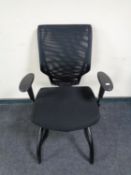 An office adjustable armchair upholstered in a black mesh fabric.