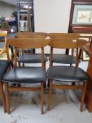 A set of four mid 20th century teak dining chairs upholstered in black vinyl.