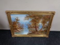 A gilt framed oil on canvas depicting a river through a wooded landscape.