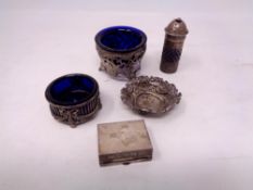 An ornate silver salt with blue glass liner, another similar salt, silver repousse dish,