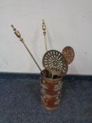 An ornate copper umbrella stand containing brass fire poker,