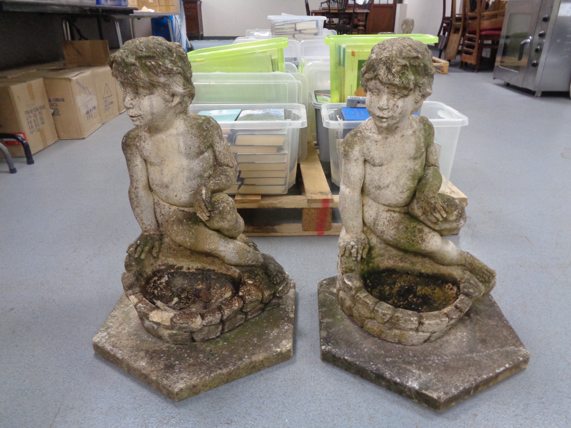 A pair of weathered concrete figures of seated children on hexagonal bases