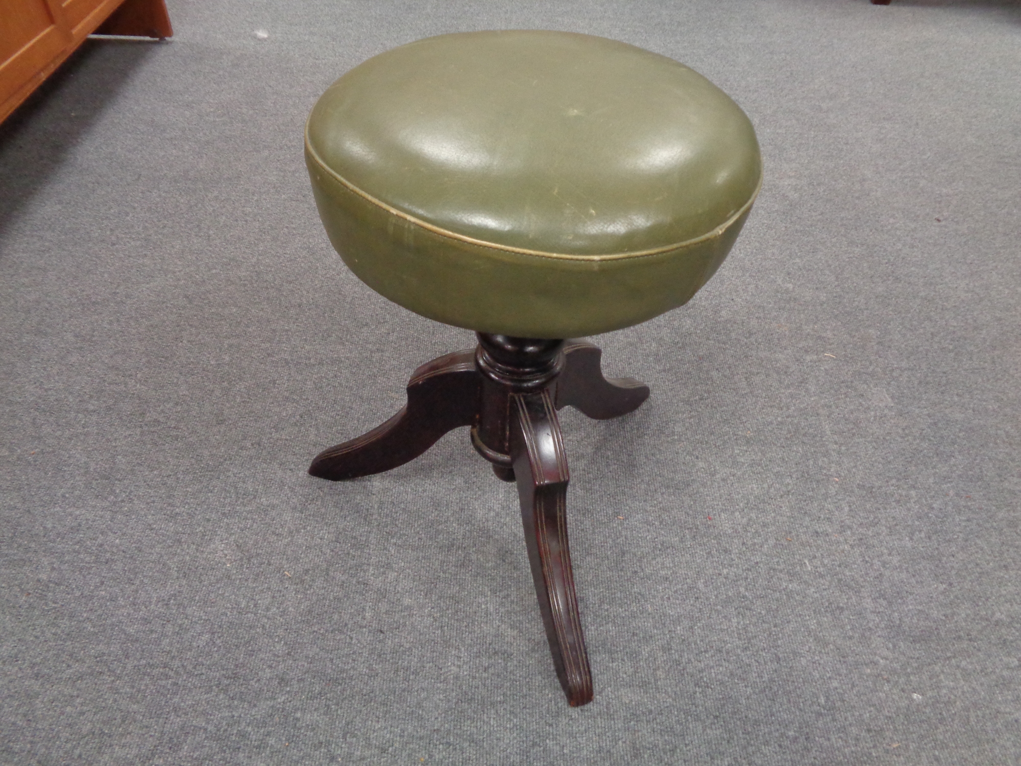 An antique mahogany revolving stool upholstered in a green leather