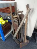 A wooden carry box containing vintage hand saws, pick axe, axe,