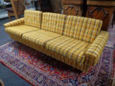 A mid 20th century three seater settee upholstered in a mustard checked fabric on teak legs