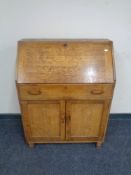 A 1930's oak bureau fitted drawer and double door cupboard beneath