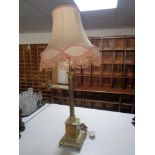 A brass Corinthian column table lamp with pink tasseled shade