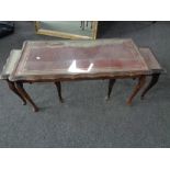 A nest of three glass topped tables with red leather inset panels