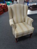 A wingback armchair on Queen Anne legs upholstered in a cream and beige striped fabric