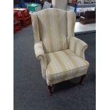 A wingback armchair on Queen Anne legs upholstered in a cream and beige striped fabric