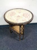 A two tier wicker and glass topped occasional table with embroidered top