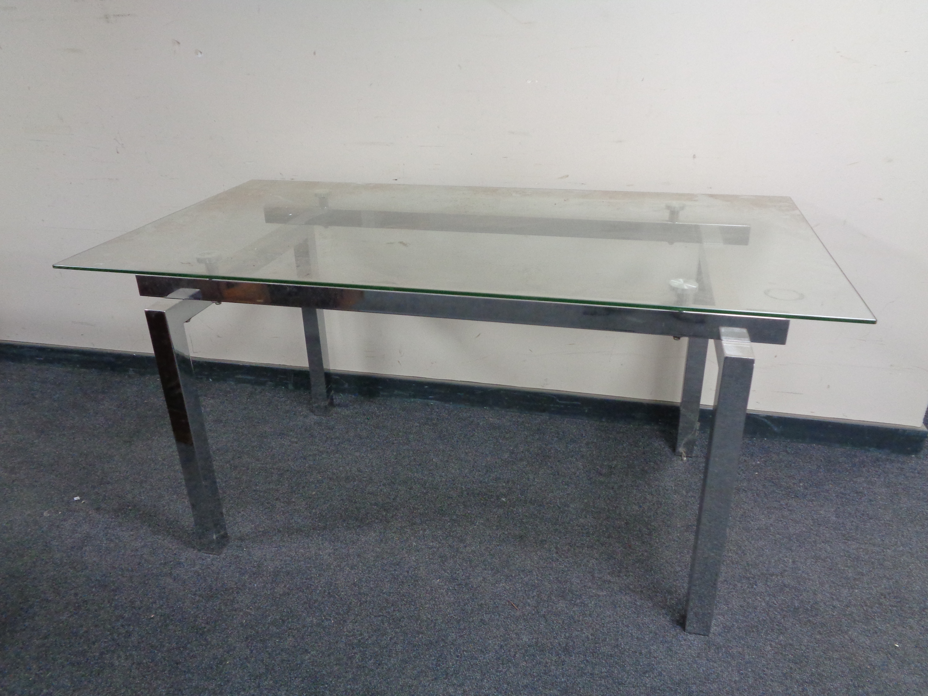 A contemporary chrome dining table with glass top