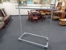A metal adjustable shop clothes rail with glass shelf