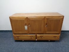 An Ercol elm and beech triple door sideboard fitted two drawer beneath on castors