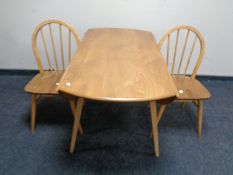 An Ercol elm and beech circular drop leaf table and two spindle back chairs