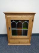 A blond oak wall mounted cabinet with leaded glass door fitted a drawer