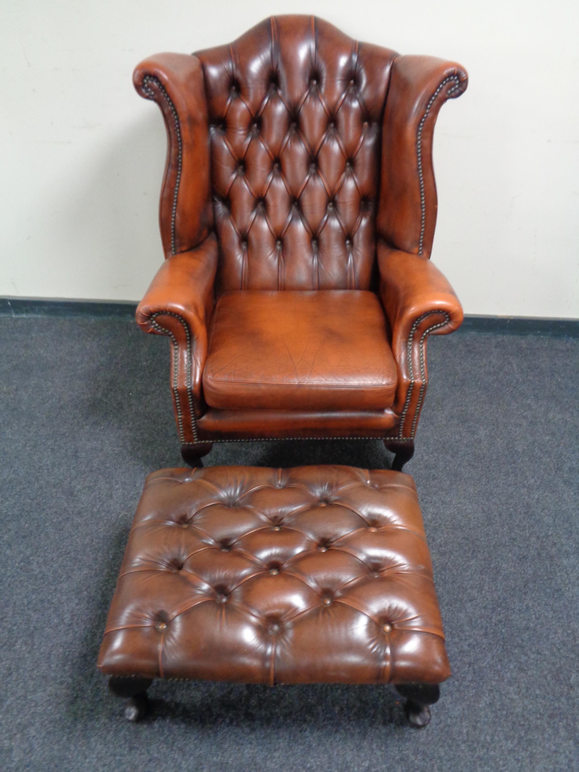 A brown buttoned leather Chesterfield wingback armchair with matching foot stool