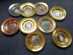 A box containing nine circular brass framed wall plates containing portrait prints