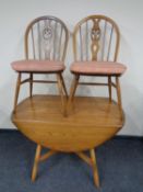 An ercol elm drop leaf dining table together with a pair of spindle back chairs with cushions