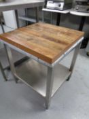 A wooden topped chopping table on a stainless steel stand