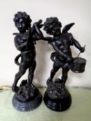 A pair of bronze figures of putti playing violin and drum, on circular black marble bases.