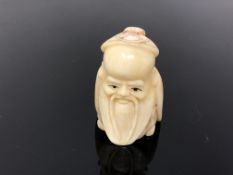 A carved bone netsuke - bearded man wearing a cap