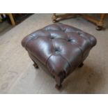 A brown button leather footstool on legs