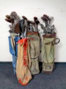 Four 20th century golf bags containing a quantity of vintage irons and drivers