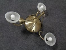 A contemporary brass hanging ceiling light with three opaque glass shades