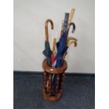A beech wood stick stand containing a quantity of assorted walking sticks and umbrellas