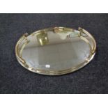 An oval contemporary mirrored serving tray with brass handle and gallery