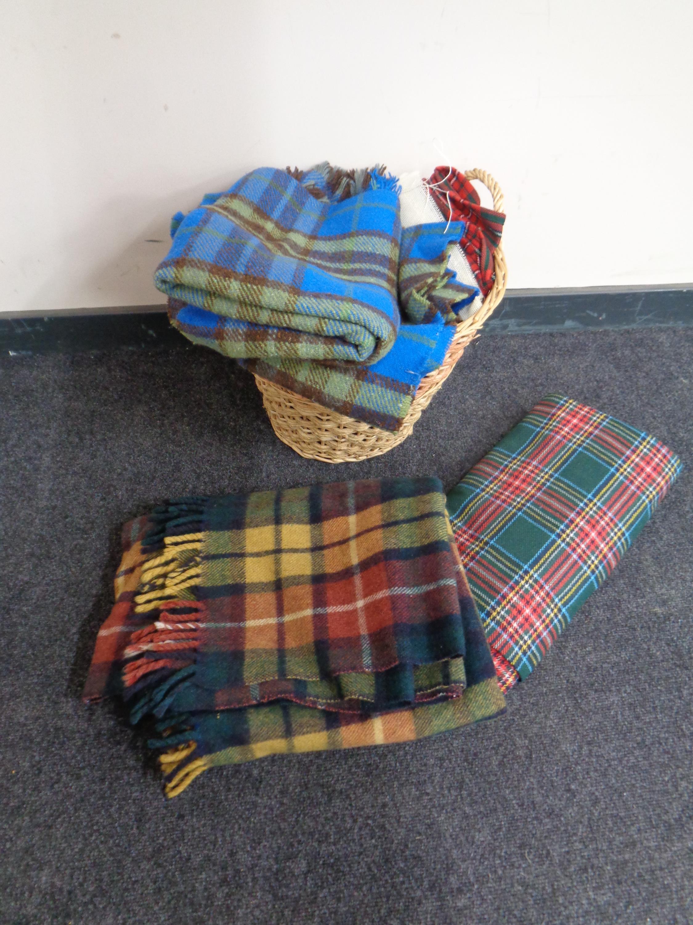 A wicker twin handled log basket containing a quantity of woolen tartan blankets