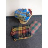 A wicker twin handled log basket containing a quantity of woolen tartan blankets