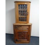 An Arts and Crafts corner cabinet with a carved panel door together with a further wall mounted