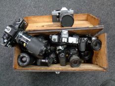 A wooden storage box containing various cameras and lenses including Praktica, Canon,