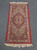 A machine made fringed Persian design rug on red ground,